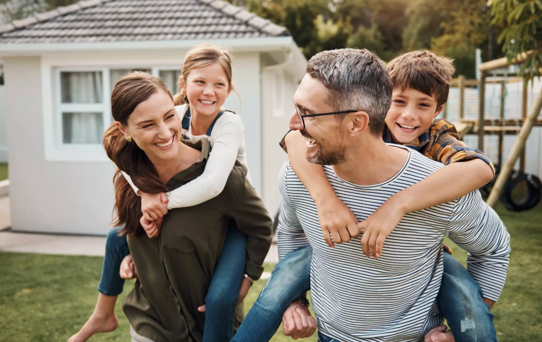 Mutter und Vater mit Tochter und Sohn Huckepack im Garten vor ihrem Haus