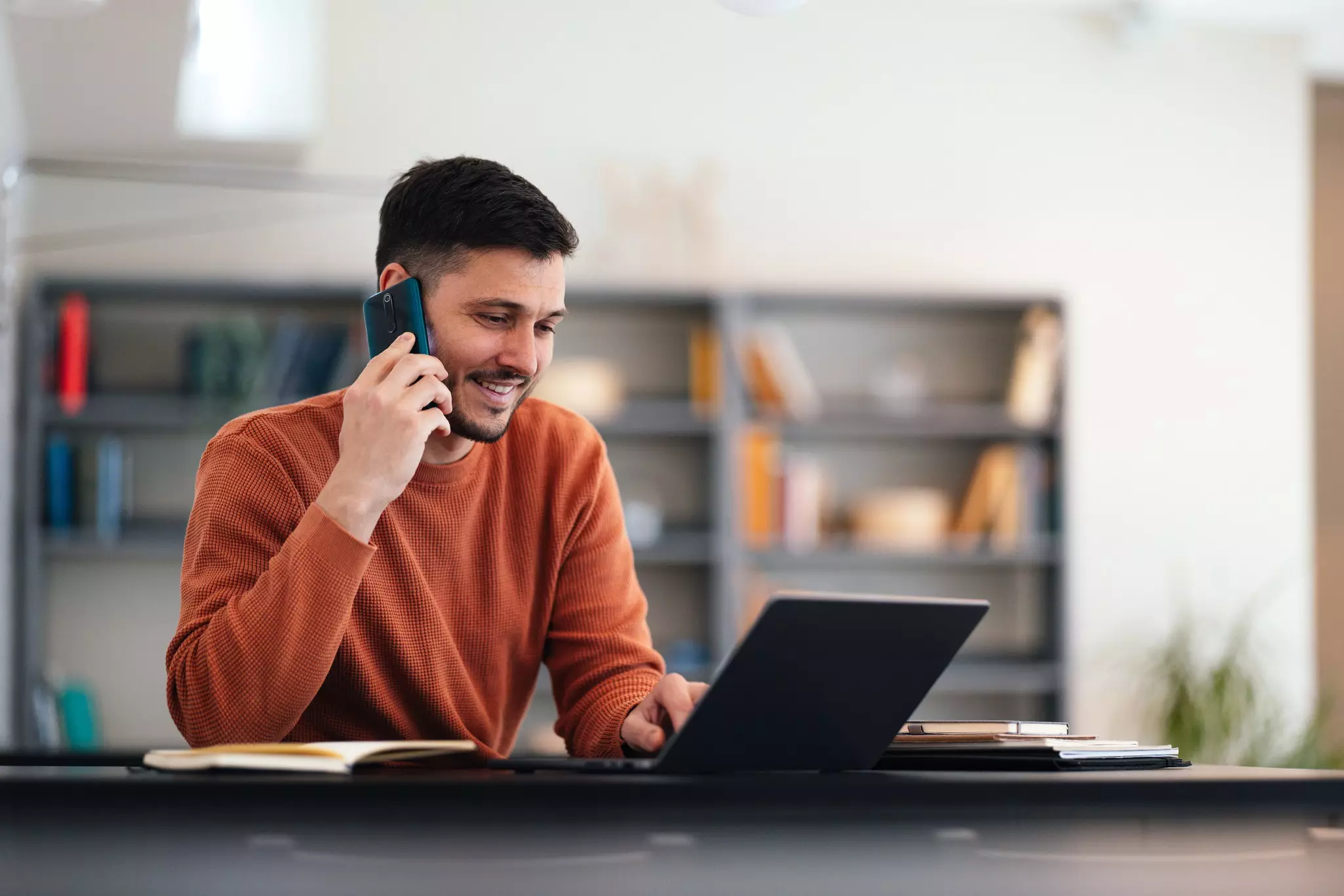 Telefonierender Mann, der am Schreibtisch vor seinem Laptop sitzt