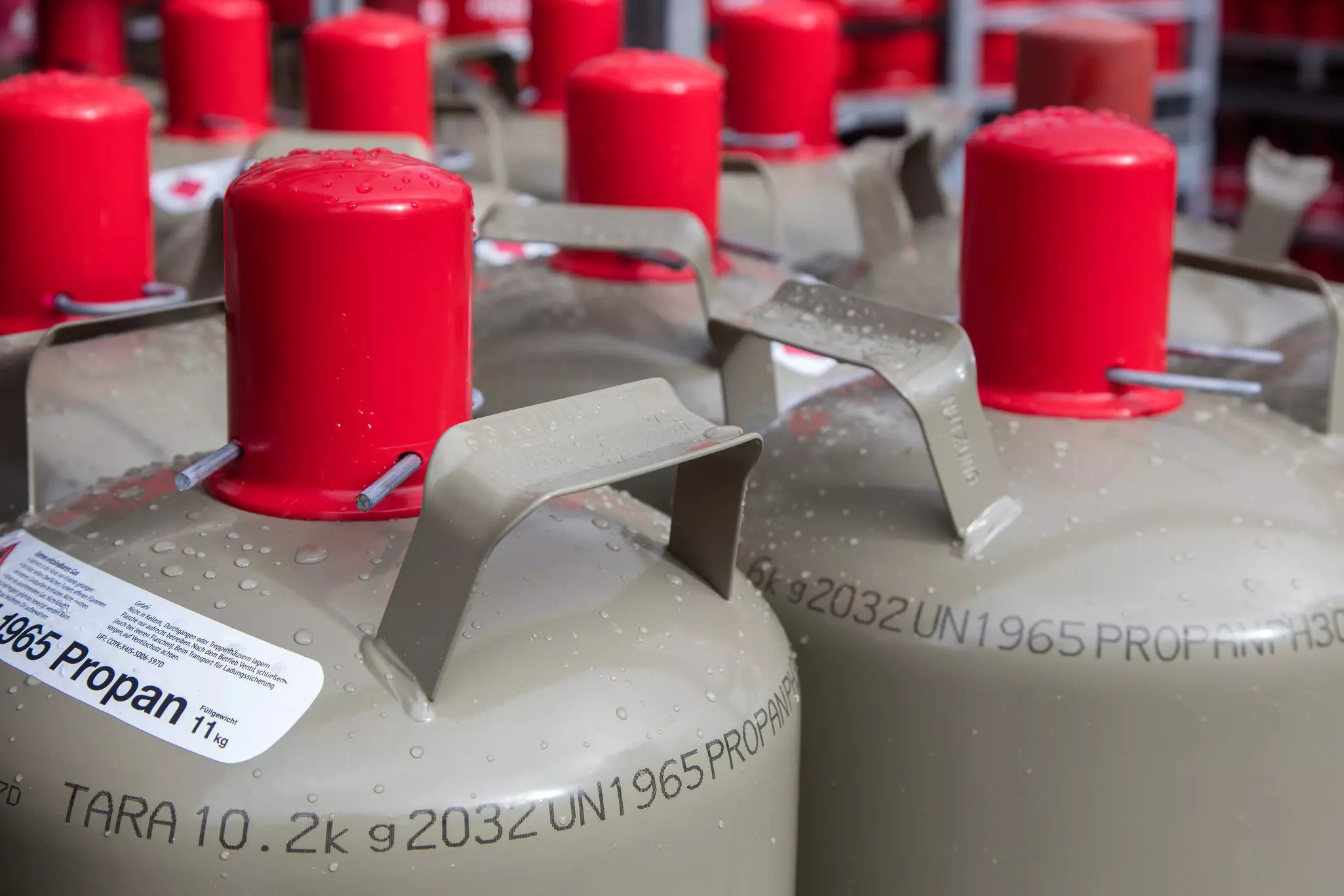 Flaschengas - Nahaufnahme mehrerer grauer Gasflaschen mit Regentropfen auf der Oberfläche
