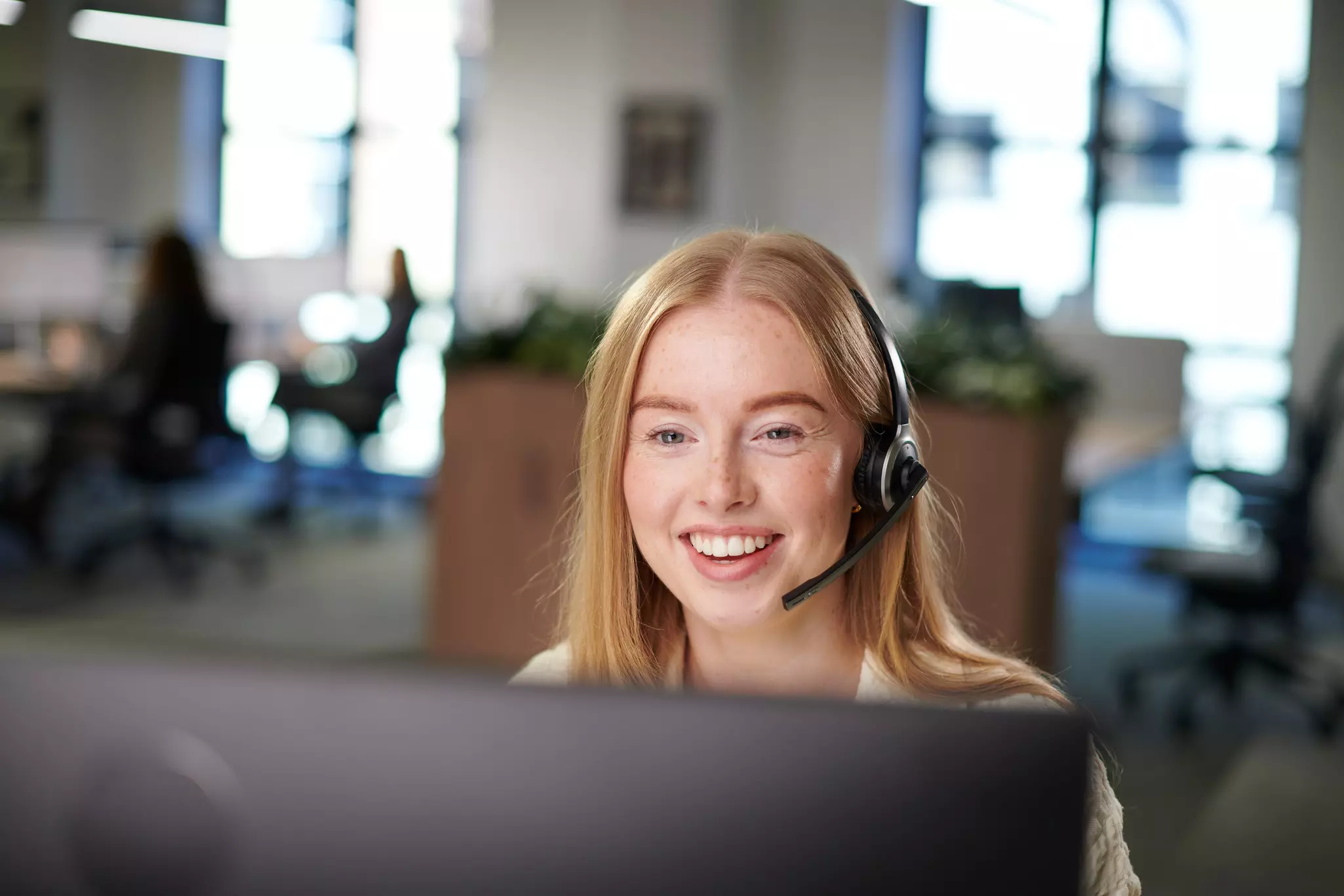 Frau mit Headset vor Bildschirm im Callcenter